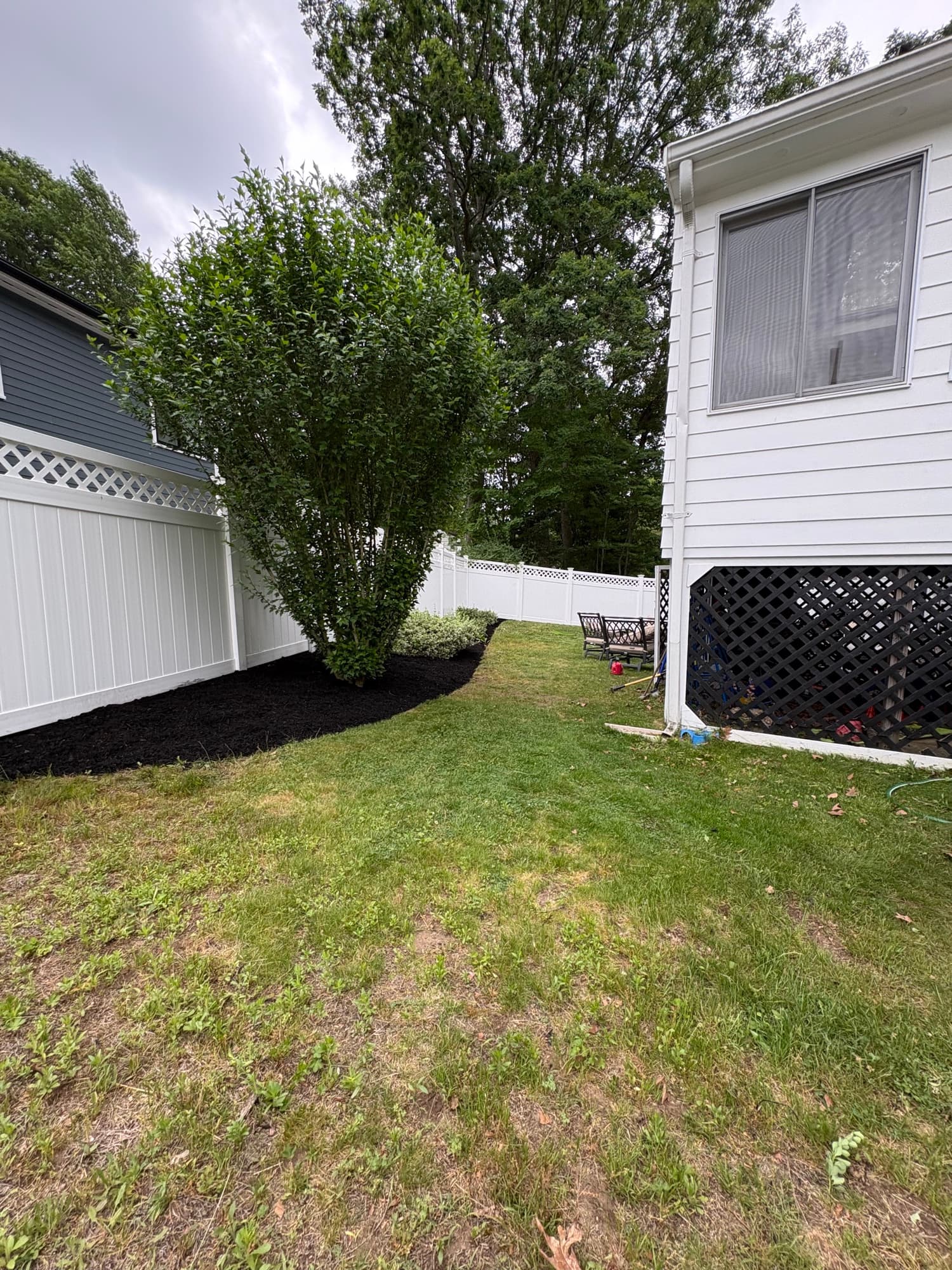 Backyard cleanup with fresh mulch beds along a white fence
